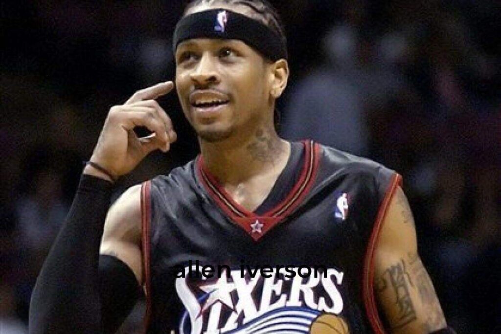 Allen Iverson, wearing a Philadelphia 76ers jersey, pointing to his head with a smile during a basketball game.