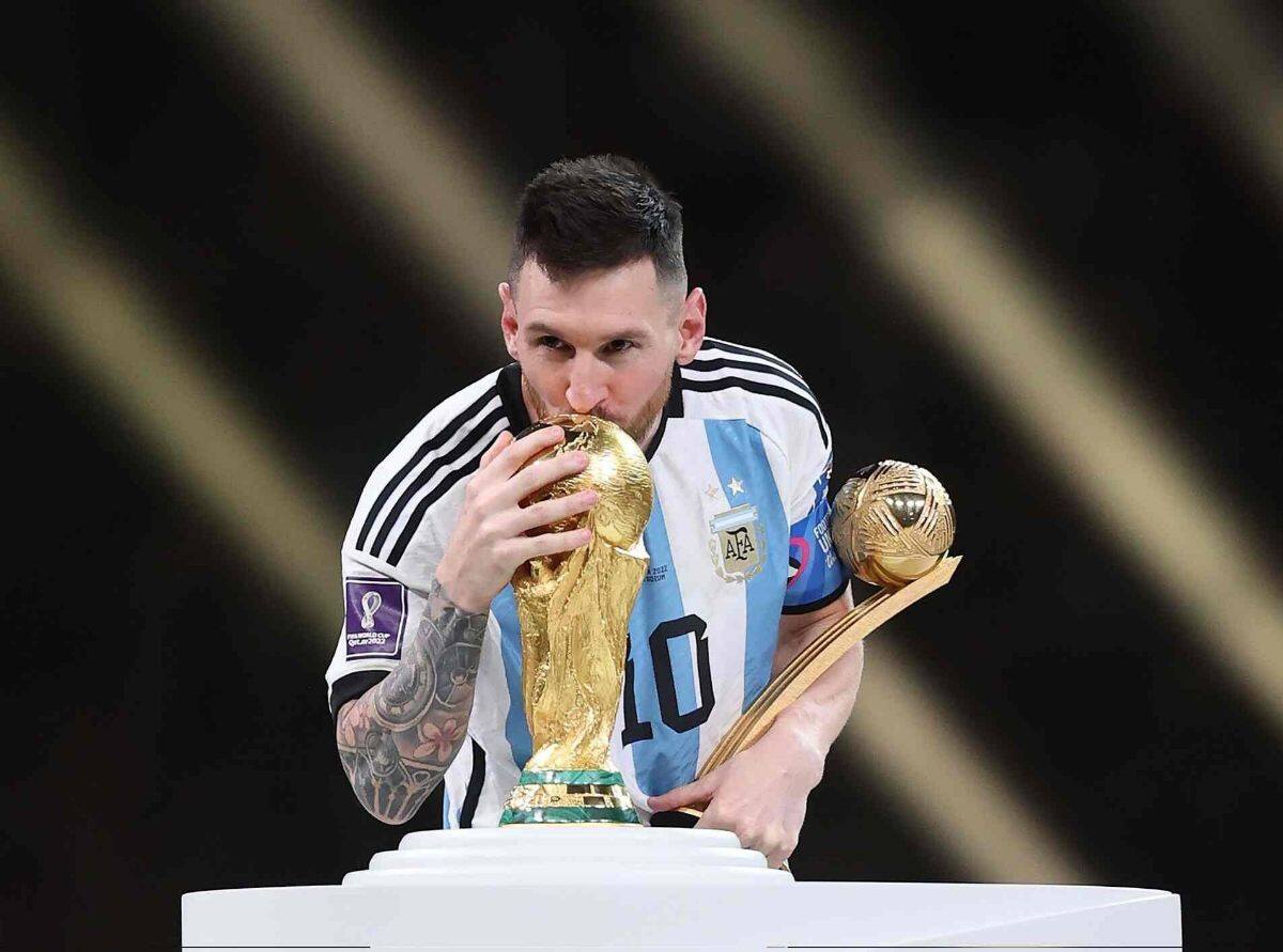 Soccer player in Argentina's blue and white jersey kisses the FIFA World Cup trophy while holding another award