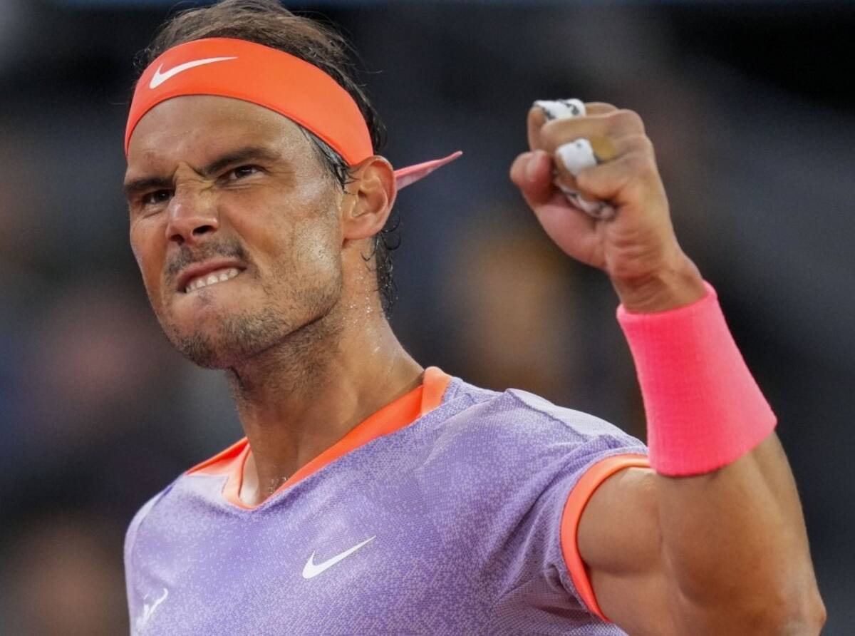 Rafael Nadal celebrating with a clenched fist, wearing a purple shirt and orange headband and wristband