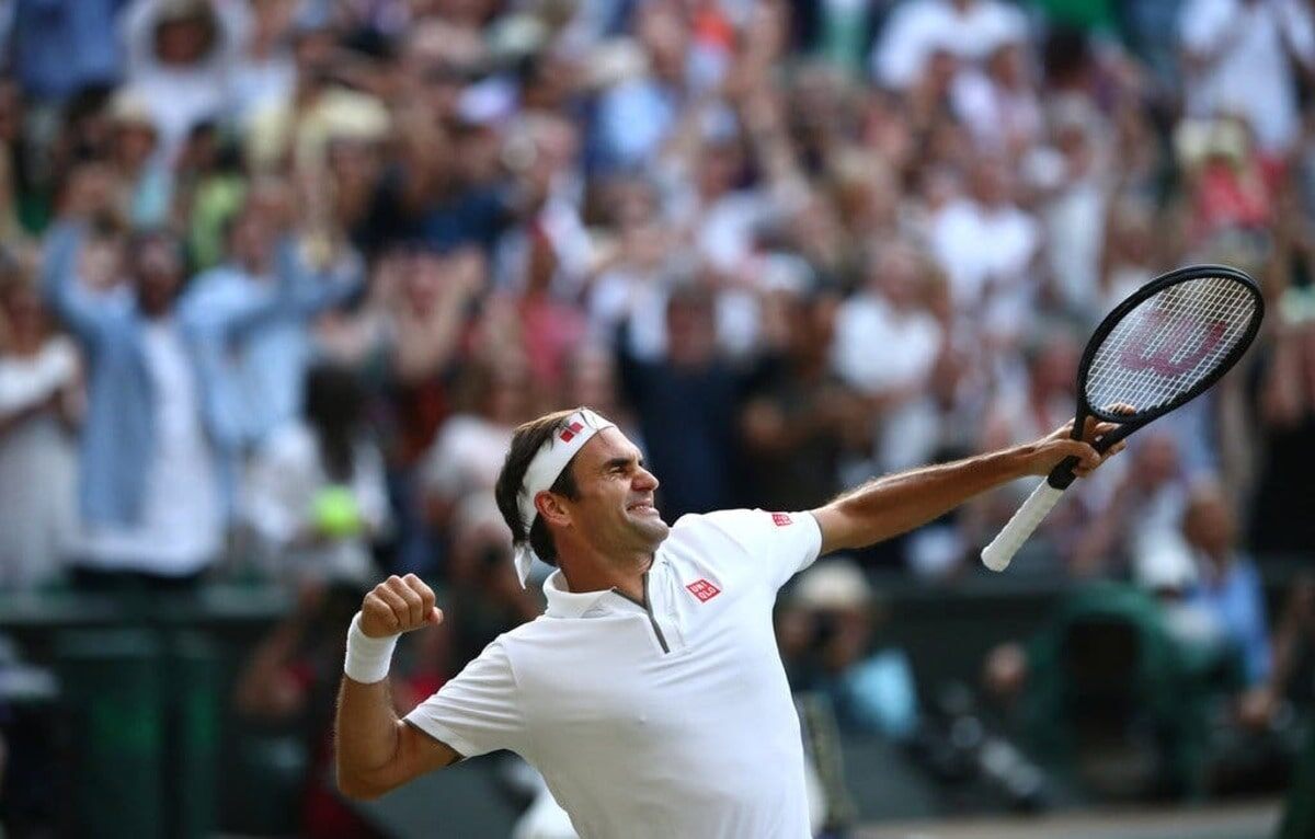A tennis player in a white outfit celebrating with a fist pump on a tennis court, with a cheering crowd in the background.